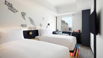 Une chambre d’hôtel avec deux lits, un bureau, une chaise, une télévision et une fenêtre donnant sur la ville.