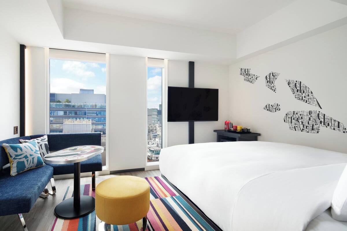 A modern hotel room with a large bed, a sofa, a small table, and a TV mounted on the wall.