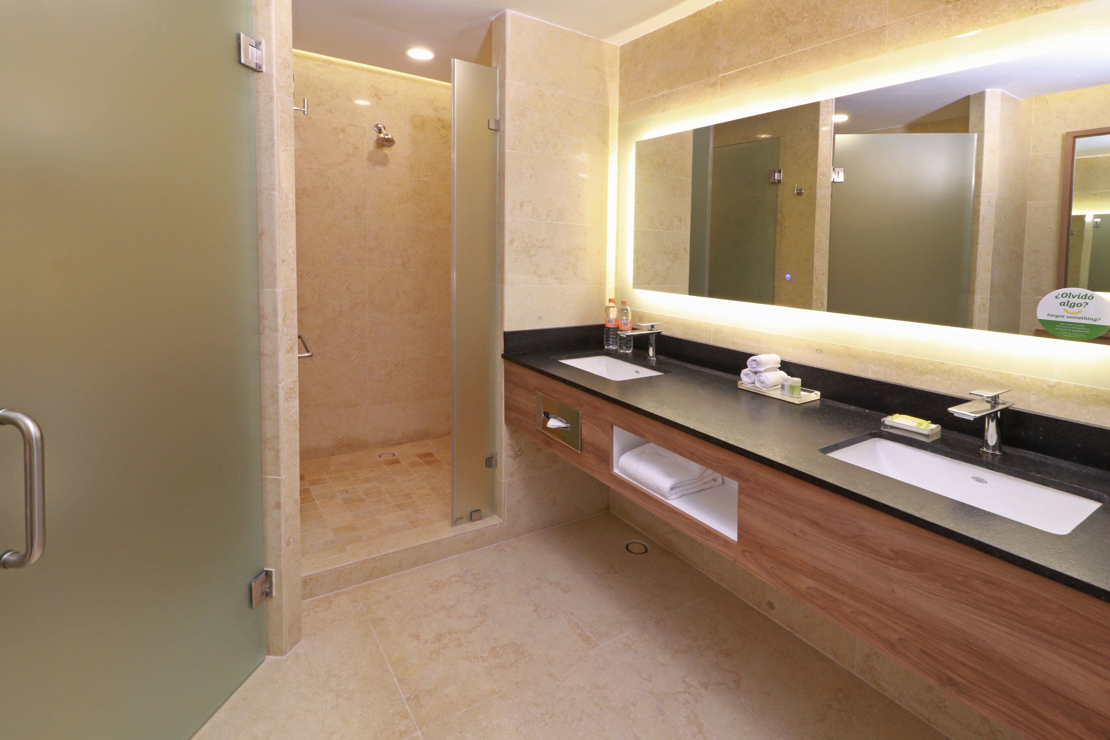 A modern bathroom with a glass-enclosed shower, two sinks, and a large mirror with integrated lighting.