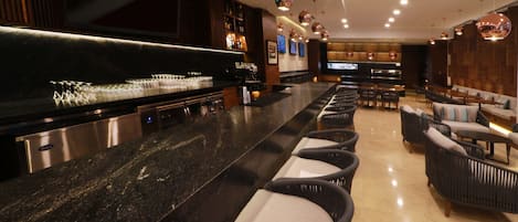 Zona de bar con una barra larga, asientos con sillones acolchados y una decoración interior moderna.