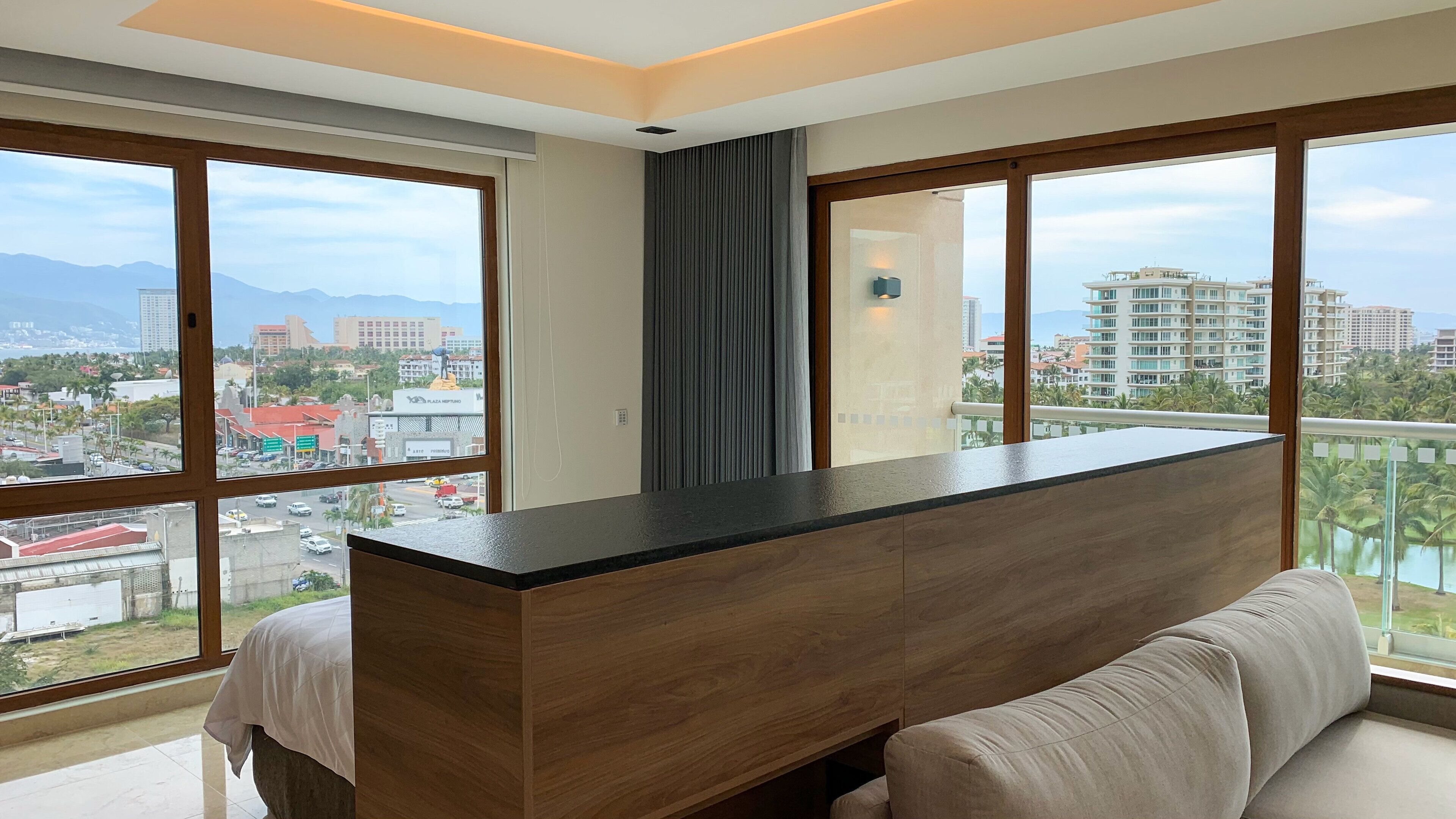 Una habitación de hotel moderna con un ventanal grande, un escritorio de madera y un sofá.