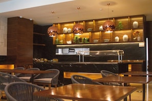 A modern restaurant with wooden tables and chairs, a black marble counter, and decorative vases on shelves. - Holiday Inn & Suites Puerto Vallarta Marina & Golf by IHG (Puerto Vallarta)