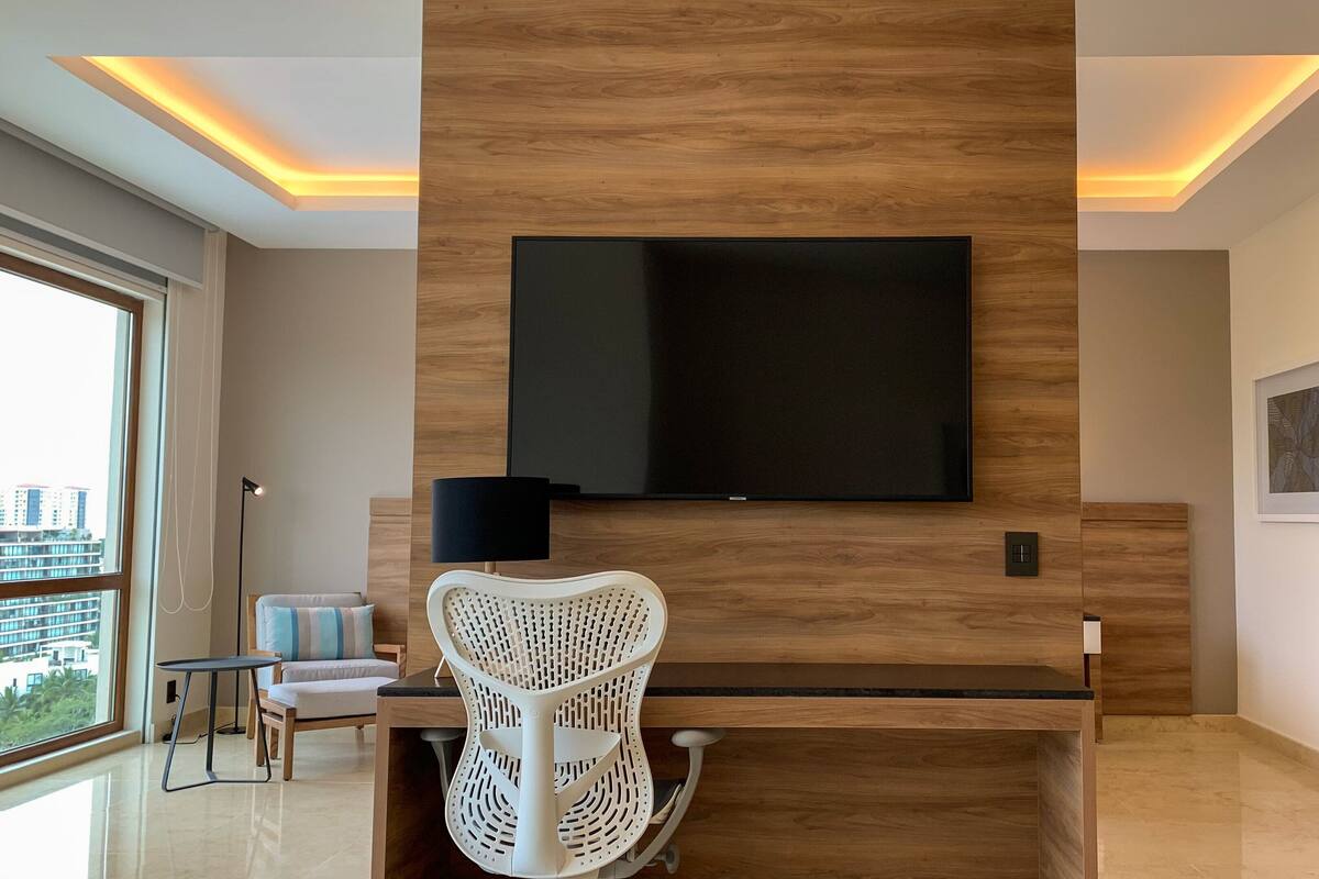 Un salon moderne avec un téléviseur à écran plat fixé à un mur en bois, une chaise en osier blanche, une petite table et un canapé.
