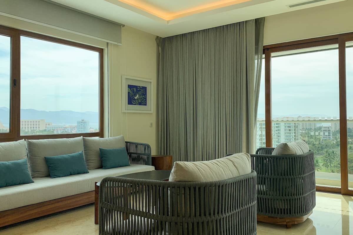 Un salon moderne avec un canapé, deux fauteuils et une grande fenêtre donnant sur la ville.