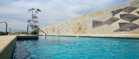 Una piscina al aire libre, sombrillas, sillones reclinables de piscina