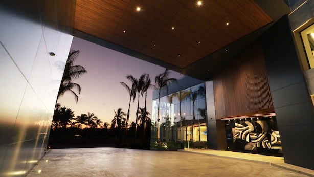 A modern building with a glass facade, palm trees, and a patterned wall.