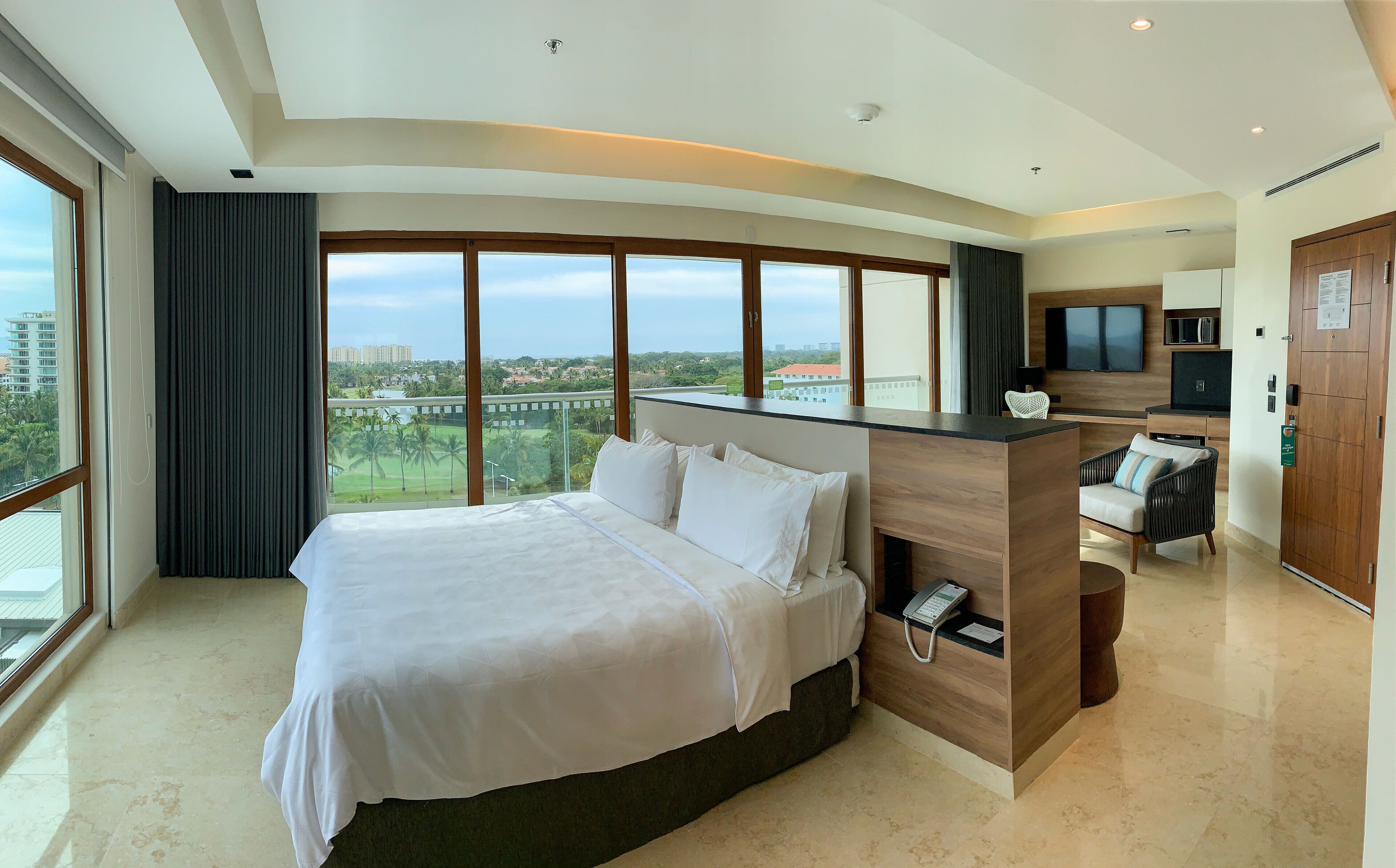 A modern hotel room with a large bed, a desk, a flat-screen TV, and a view of the cityscape.