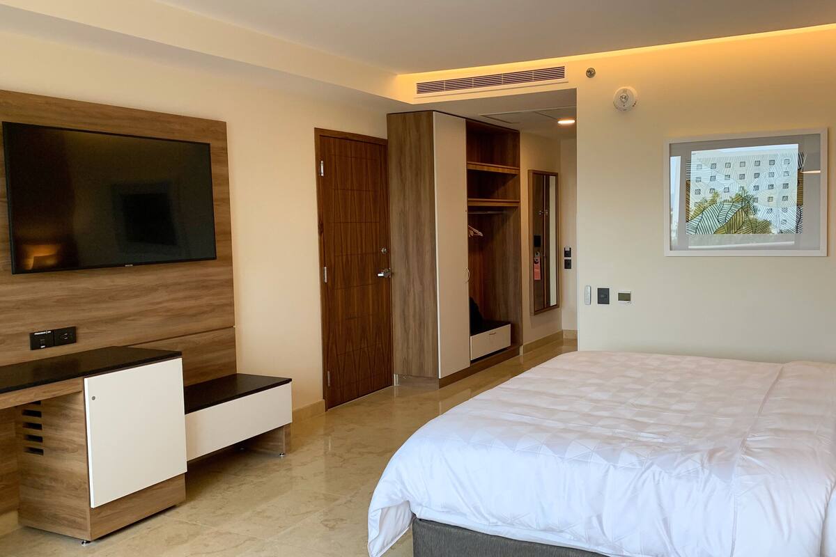 Une chambre d’hôtel avec un grand lit, un téléviseur fixé au mur, une armoire et une petite fenêtre donnant sur le paysage urbain.