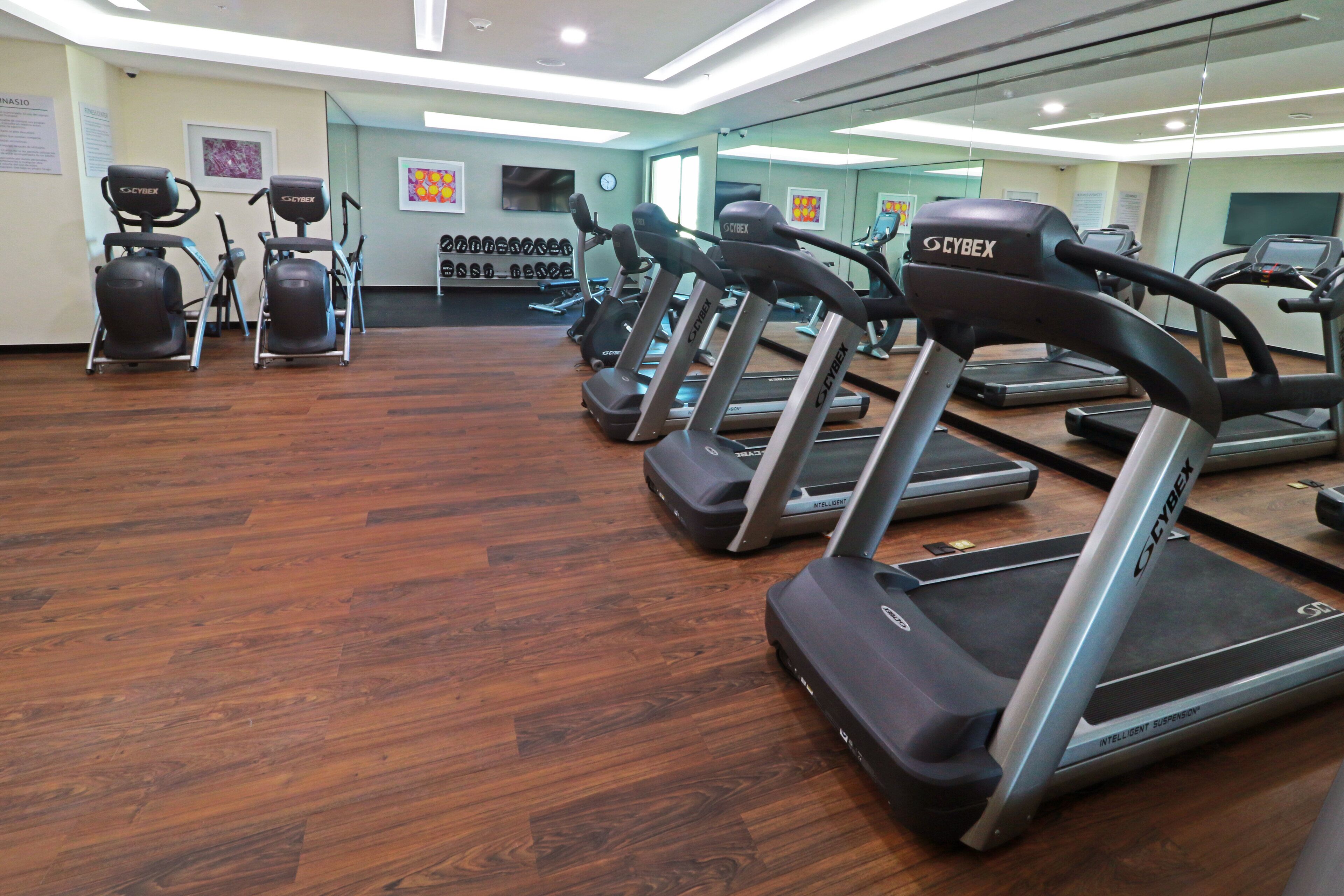 Un gimnasio con cintas de correr, bicicletas estáticas y elípticas.