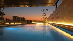 An indoor swimming pool with a sunset view, a covered roof, and a decorative wall.