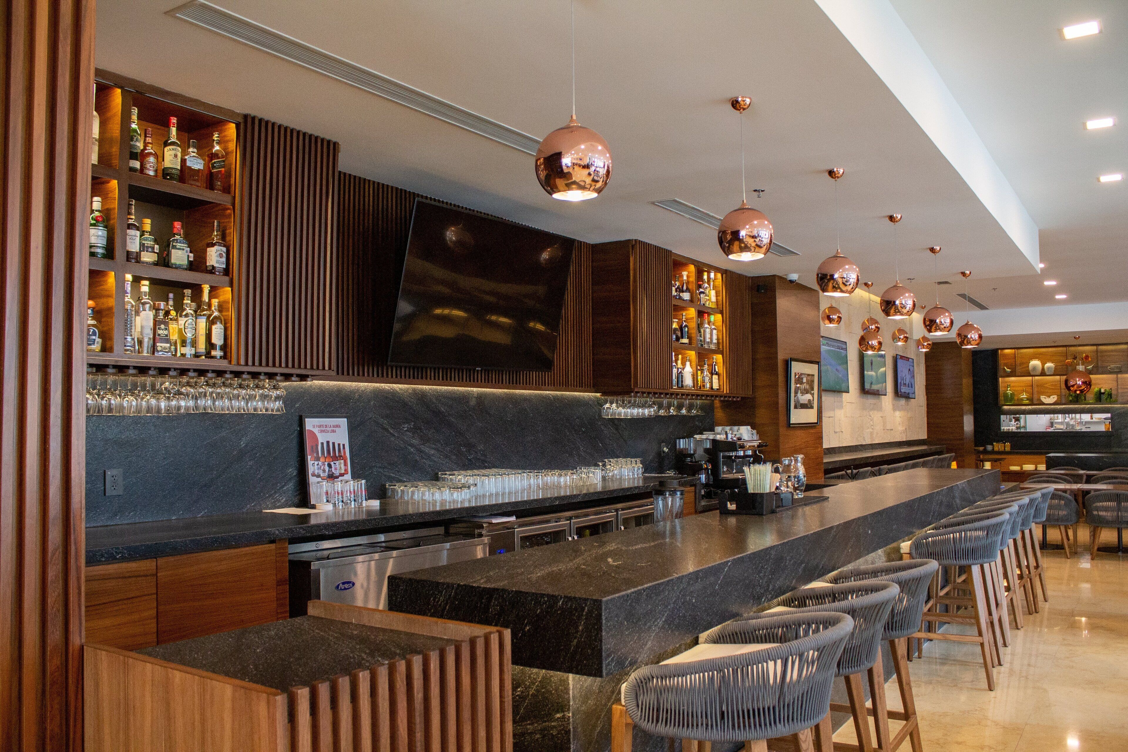 Un espace bar moderne doté d’un long comptoir, de tabourets et d’une variété de bouteilles et de verres.