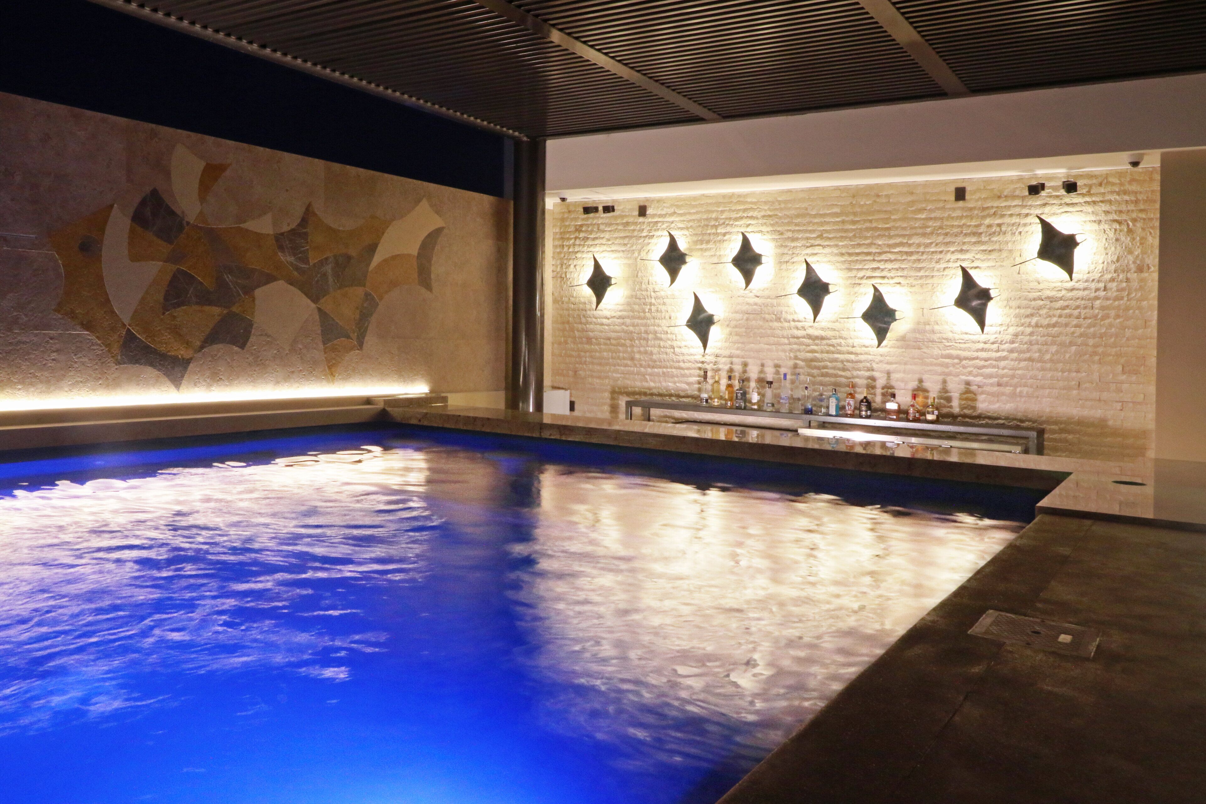 Une piscine dotée d’un mur au motif géométrique et d’un espace bar avec des bouteilles exposées.