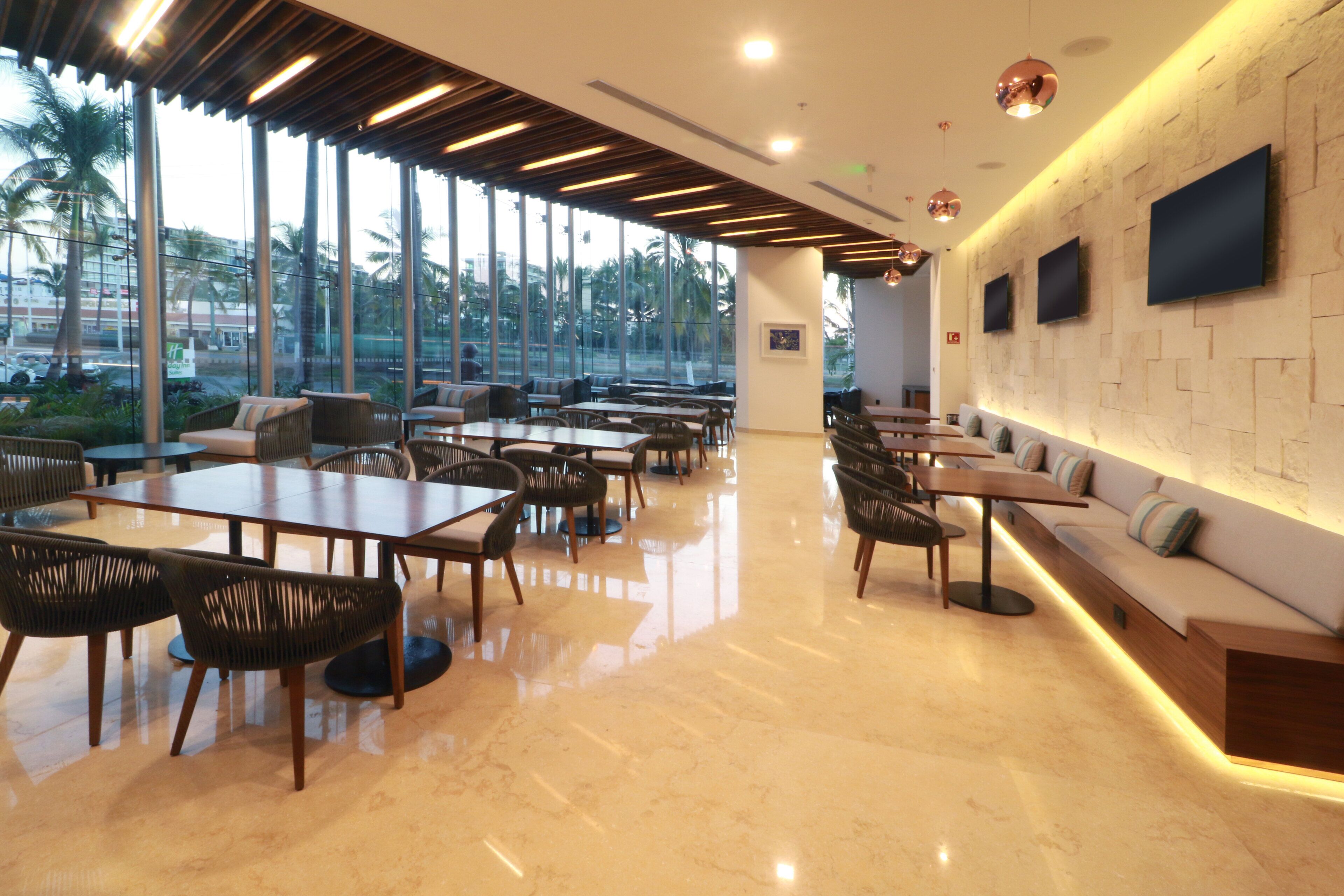 Un restaurant moderne doté d’une grande salle à manger, de larges fenêtres et d’un mur en pierre sur lequel sont fixés des téléviseurs.