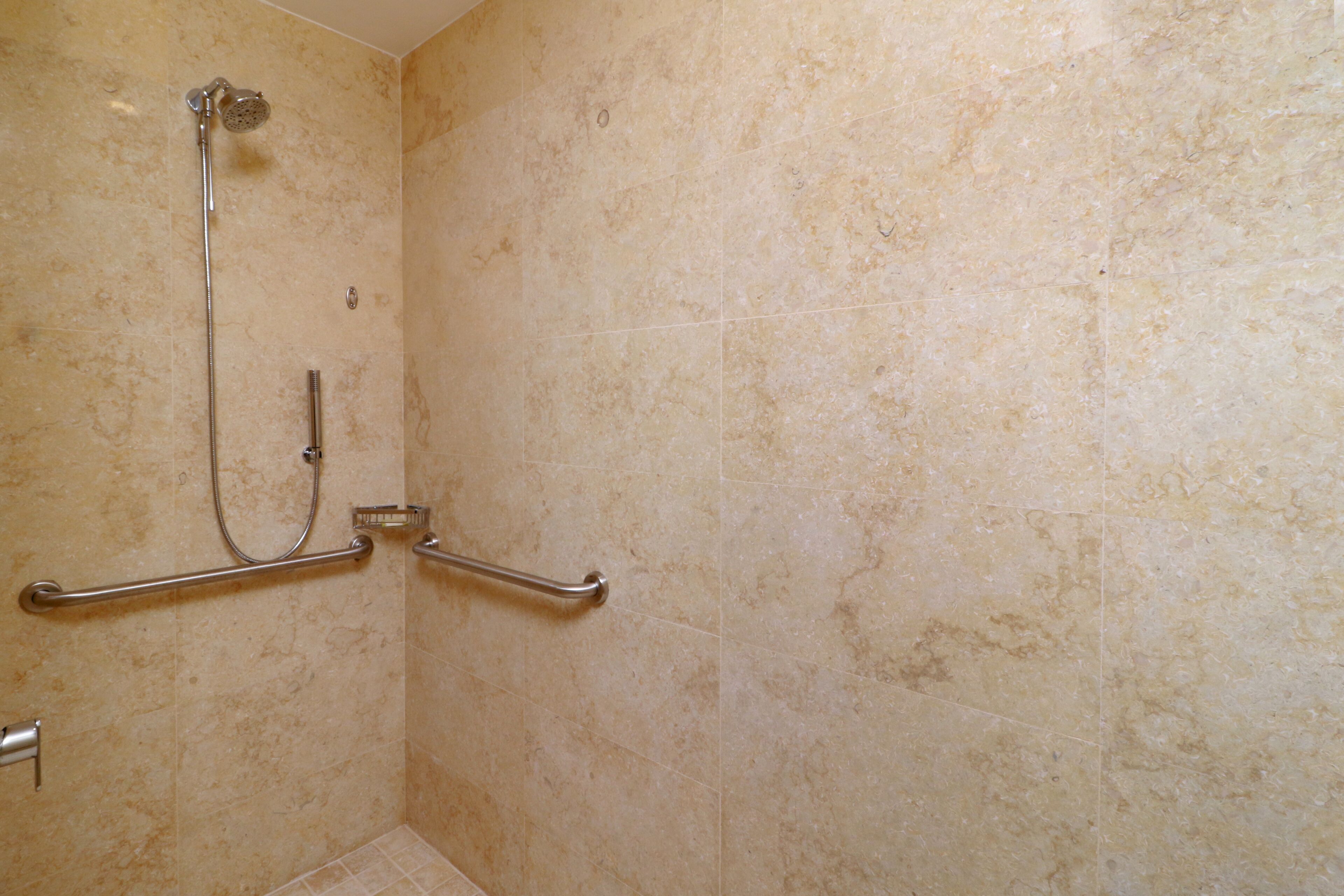 A bathroom with beige tiles, a shower with a handheld showerhead, and grab bars.