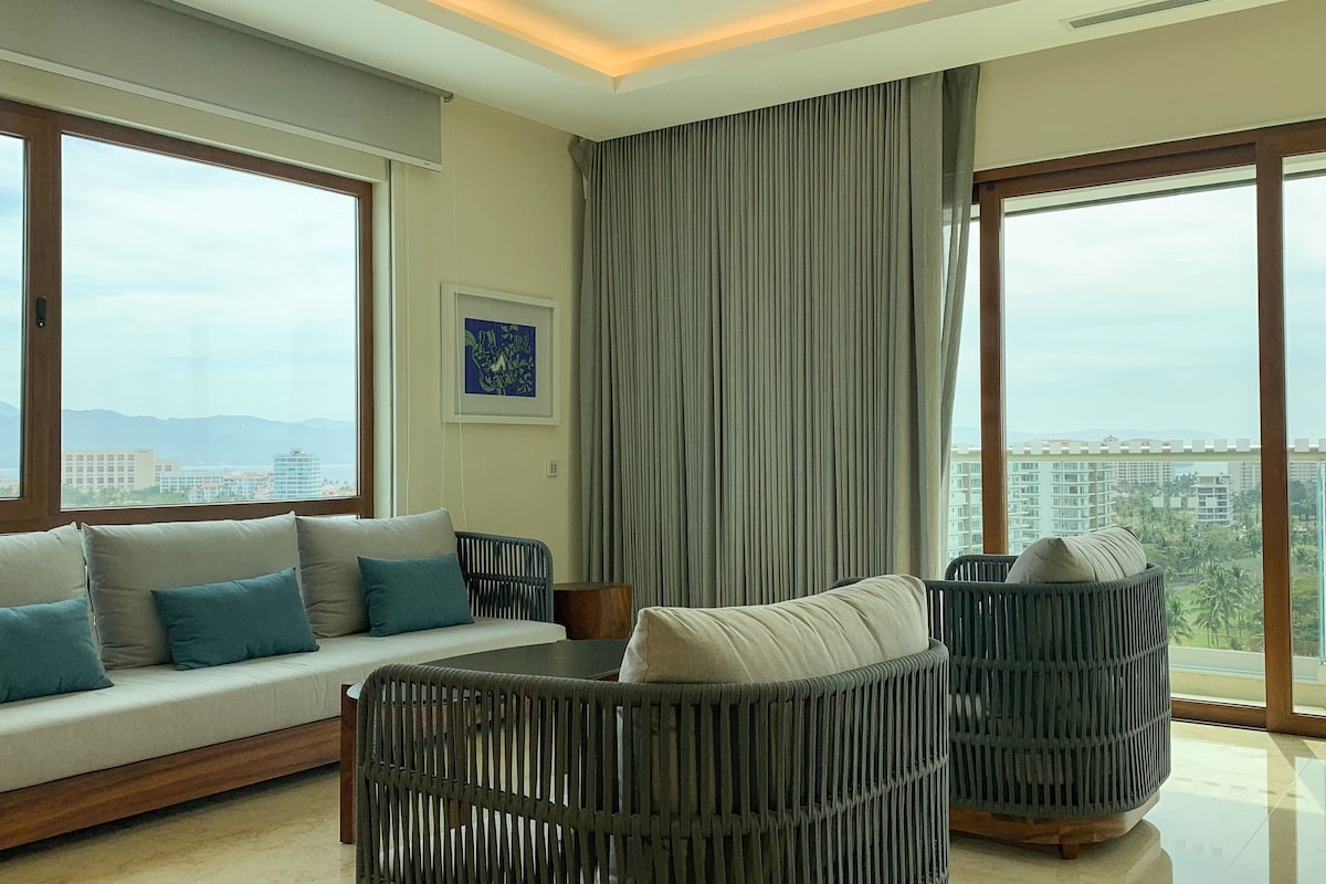 A modern living room with a sofa, two armchairs, and a large window with a view of a cityscape.