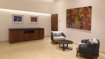 A modern lobby with a wooden reception desk, a sofa, two armchairs, and abstract art on the walls.