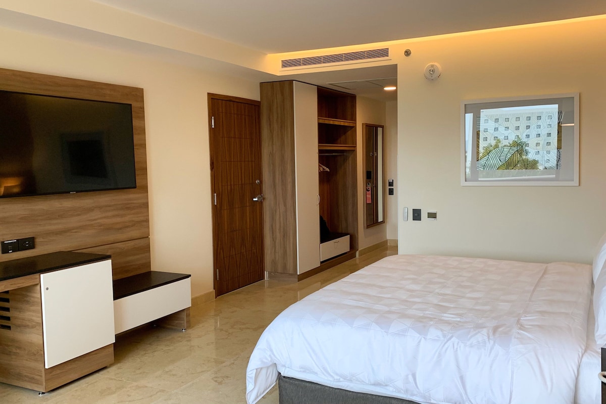 A hotel room with a bed, a TV mounted on the wall, a wardrobe, and a bedside table.