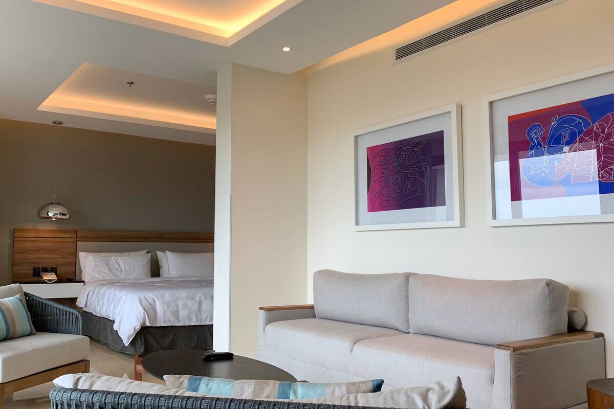Une chambre d’hôtel avec un lit, un canapé, une chaise et une table basse. Deux œuvres d’art encadrées sont accrochées au mur.