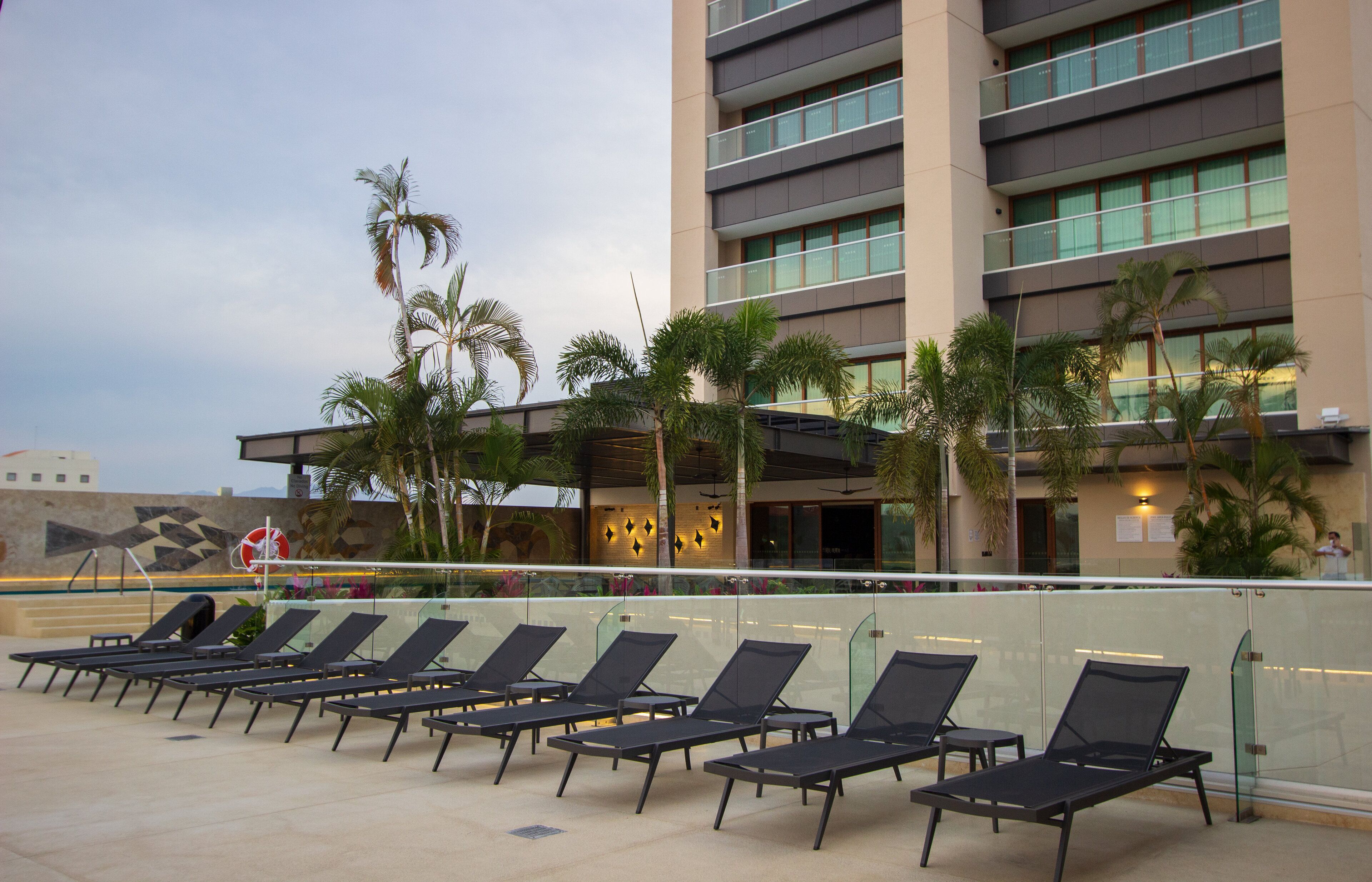 Un hotel con zona de piscina, tumbonas y palmeras.