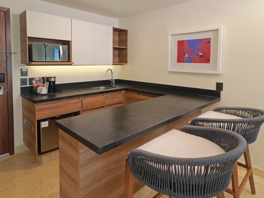 A modern kitchen with wooden cabinets, a black countertop, a built-in microwave, and two wicker chairs.