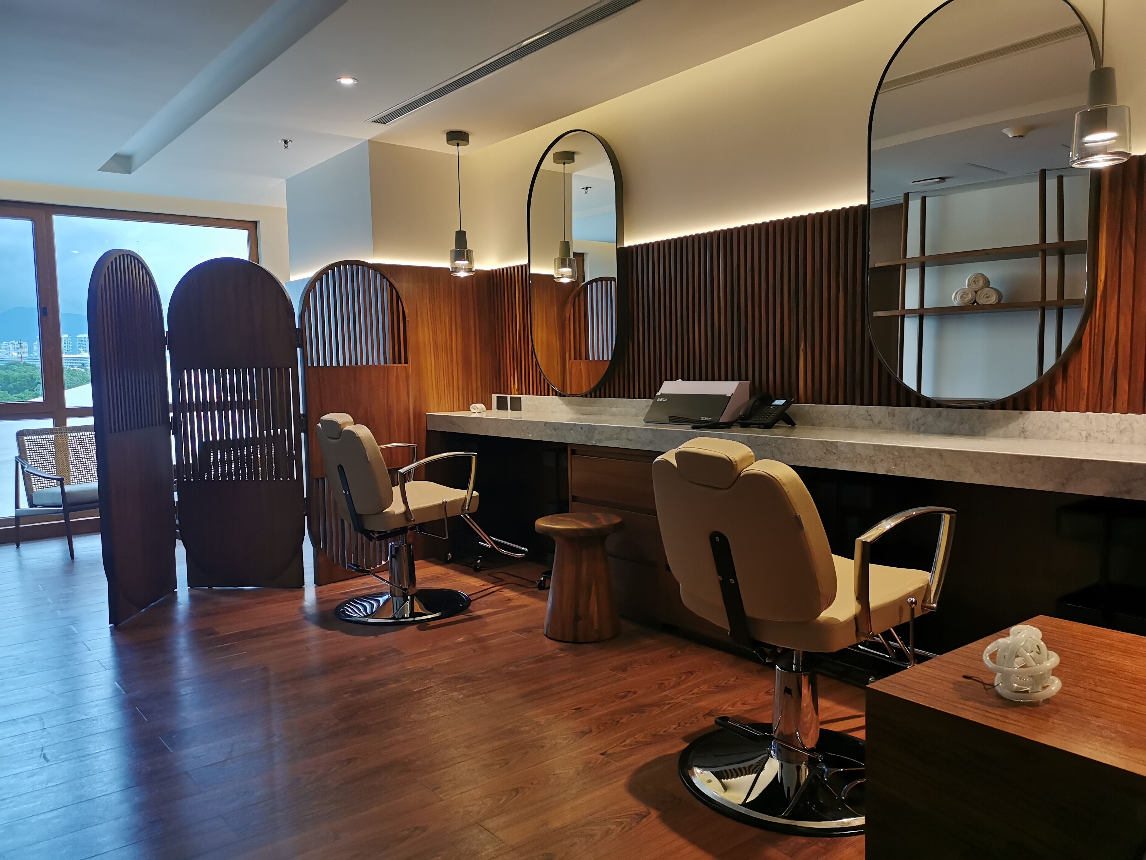 Un salon de coiffure moderne, doté de planchers en bois, de deux fauteuils de coiffure, d’un grand miroir et d’un comptoir avec un ordinateur portable et un téléphone.