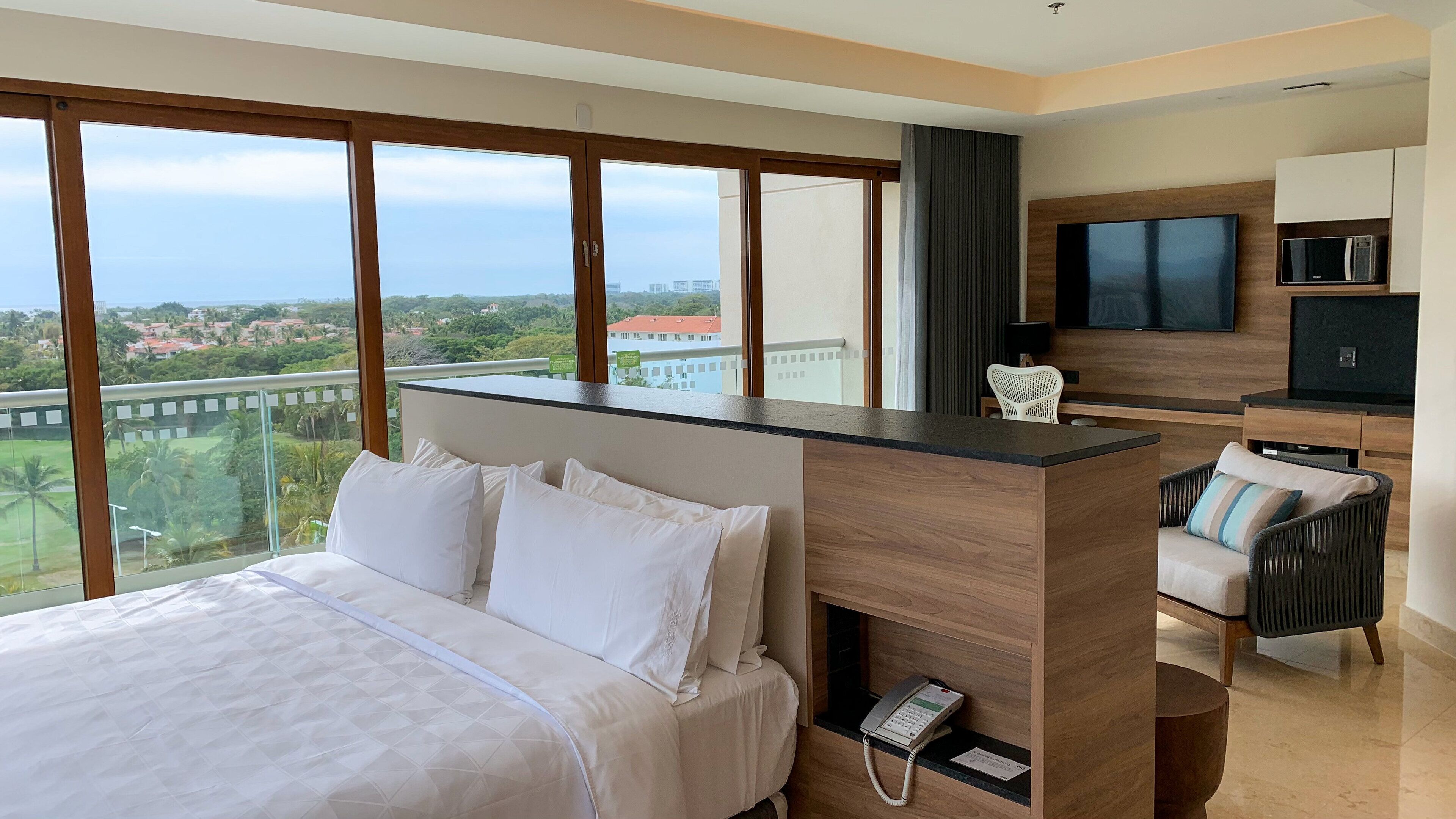 A hotel room with a large bed, a desk with a phone, a TV, and a view of the city.