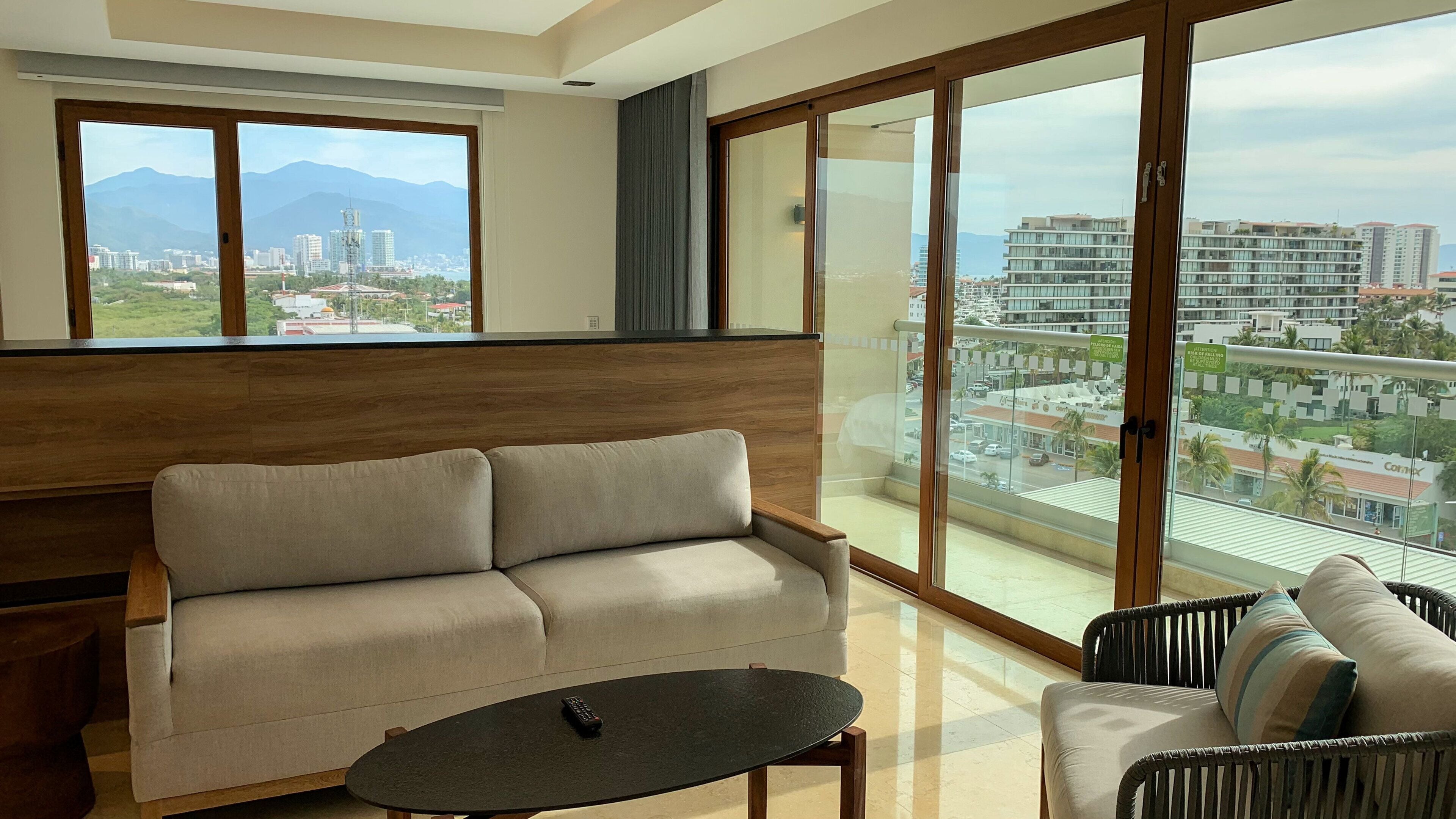 Una sala de estar moderna con sofá, una mesa de centro y vistas de un paisaje urbano a través de amplios ventanales.