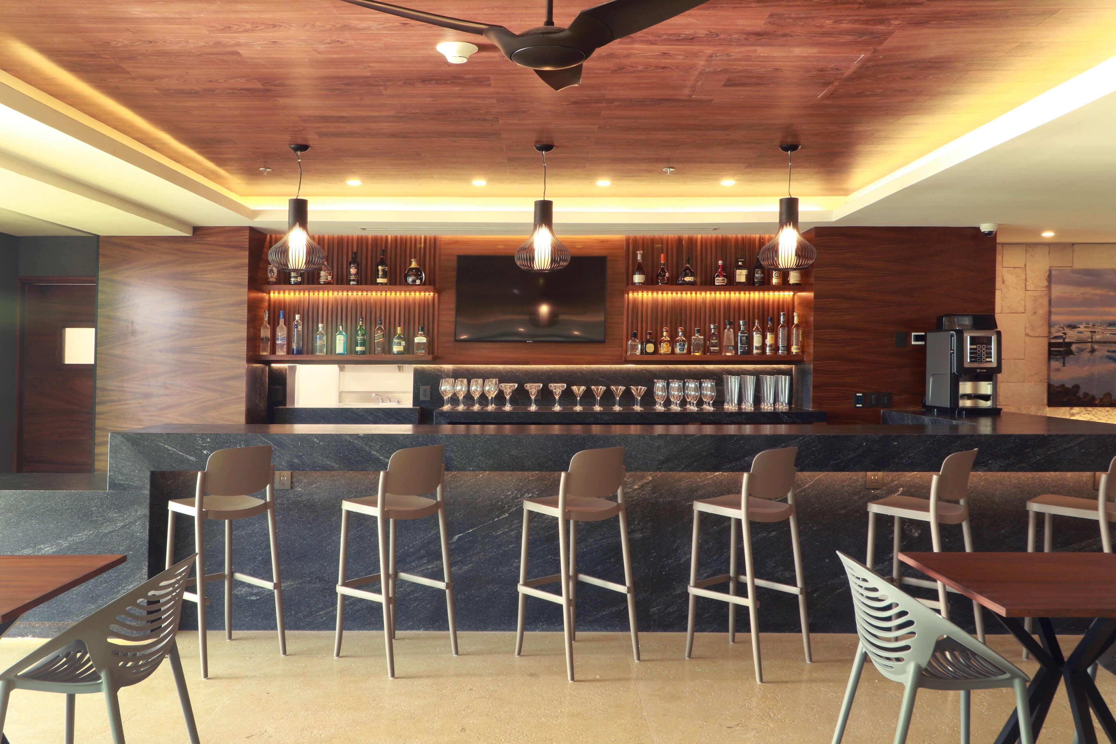 Una zona de bar con techo de madera, taburetes, un televisor en la pared y una máquina de café.