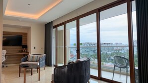 A modern living room with a large TV, comfortable seating, and a balcony with a city view.