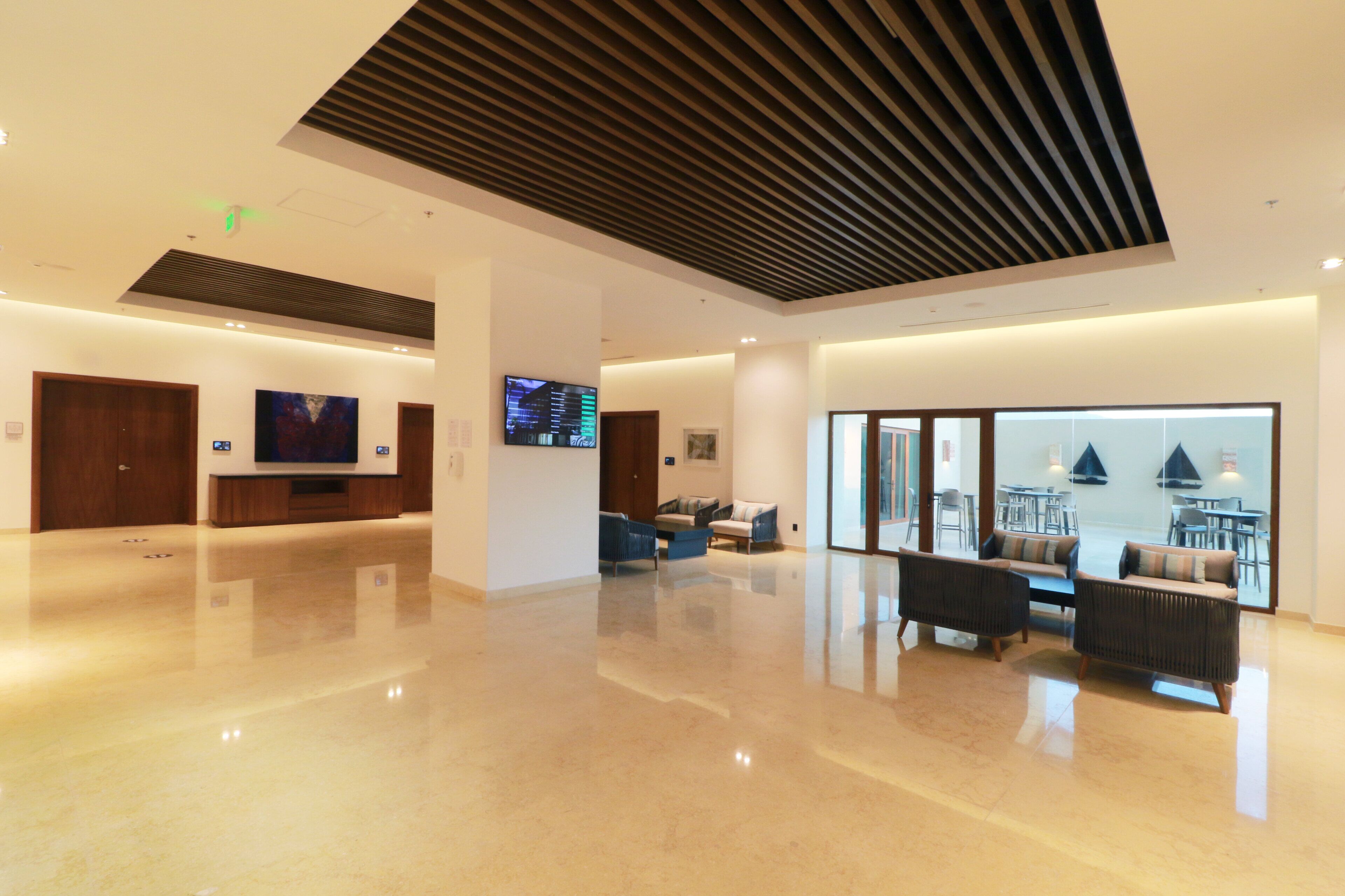 A spacious lobby with a high ceiling, a flat-screen TV mounted on the wall, and a seating area with sofas and armchairs.