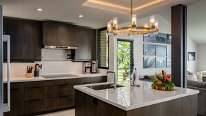 Une cuisine moderne avec des meubles de couleur bois foncé, un îlot central et un luminaire suspendu.