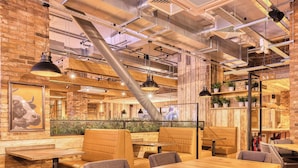 A restaurant interior with wooden tables, cushioned seating, exposed ductwork, and a brick wall. - Premier Inn Glasgow Cc St Enoch Square (Glasgow)