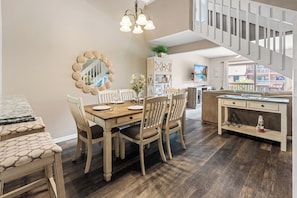 Un coin repas avec une table et des chaises en bois, un lustre, un miroir doté d’un cadre à motifs festonnés et un escalier.