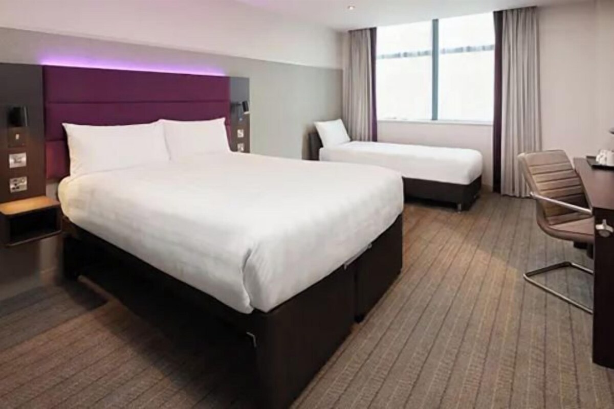 A hotel room with a large bed, a smaller bed, a desk, and a chair.
