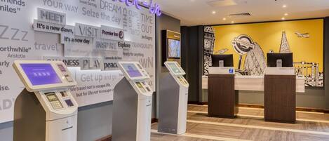 A hotel reception area with check-in kiosks, a neon sign, and a wall with motivational quotes.