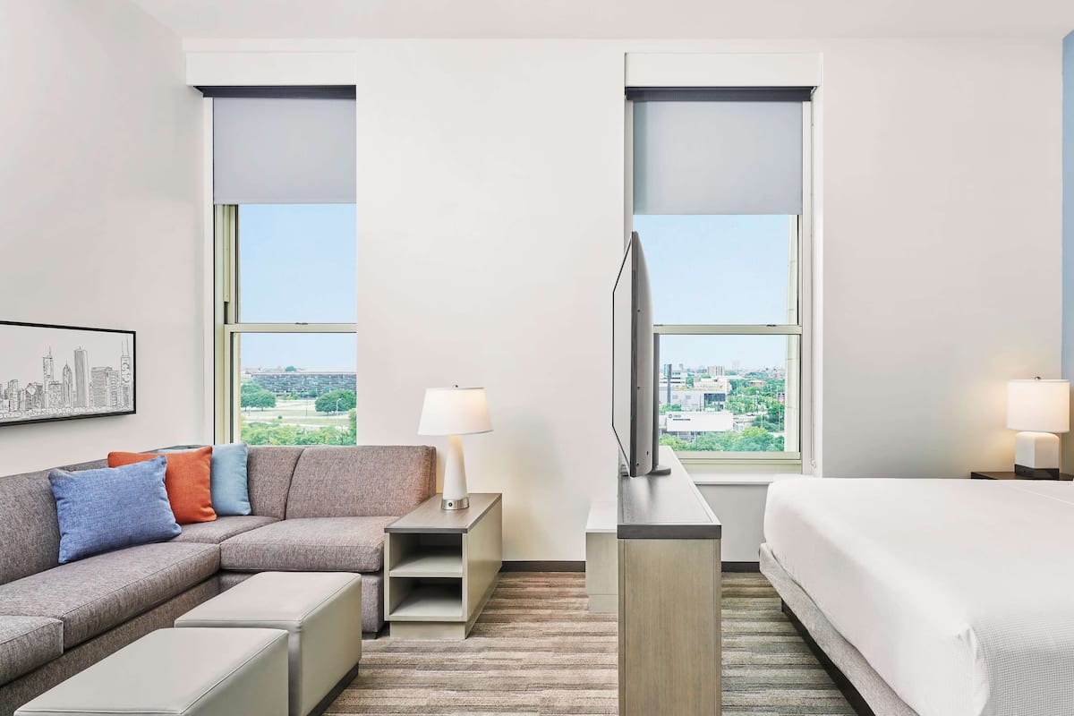 Ein modernes Hotelzimmer mit einer Couch, einem Bett, einem Fernseher und Blick auf die Stadt.