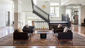 A spacious lobby with a grand staircase, modern seating, and a large window providing natural light.