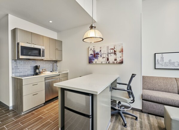 Una cocina moderna con microondas, cafetera y un lavabo. Hay un comedor con una mesa y sillas, y un sofá.
