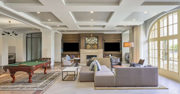 Un amplio salón con mesa de billar, asientos cómodos, chimenea y ventanas grandes.