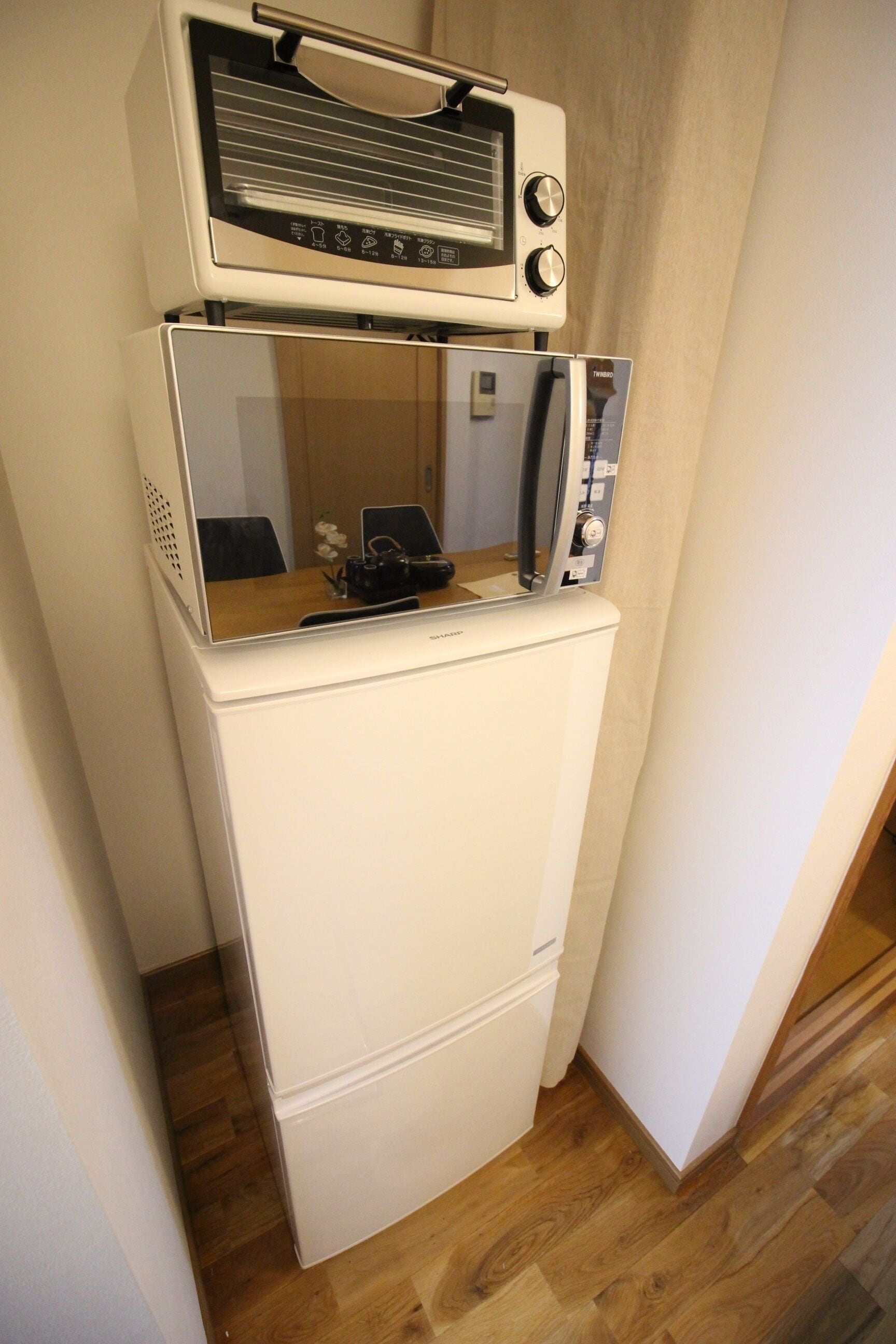 A compact refrigerator with a microwave on top, situated in a corner of a room with wooden flooring.