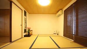 A traditional Japanese room with tatami flooring, a sliding door, a wall-mounted air conditioner, and a small potted plant. - Trad Guest House Kyoto (Kyoto)