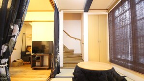 A room with tatami flooring, a tatami mat table, a television, a wardrobe, and a staircase. - Trad Guest House Kyoto (Kyoto)