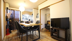 A modern kitchen with wooden cabinets, a dining table with chairs, and a TV on a stand. - Trad Guest House Kyoto (Kyoto)
