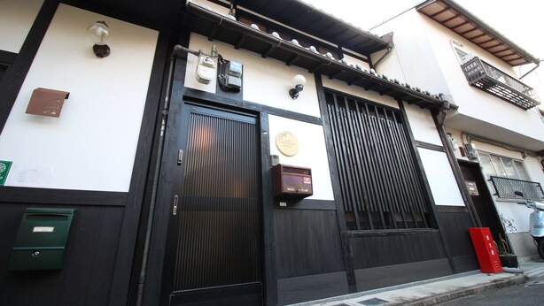 A traditional building with a black gate, a small sign, and a mailbox. - Trad Guest House Kyoto (Kyoto)