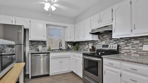 A modern kitchen with white cabinets, stainless steel appliances, and a tiled backsplash.