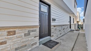 A residential building with a dark front door, stone foundation, and a small concrete pathway leading to the entrance.
