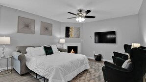 A modern bedroom with a bed, a fireplace, a TV, and a ceiling fan.