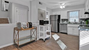 A modern kitchen with white cabinets, a stainless steel refrigerator, a coffee maker, and a microwave on a cart.