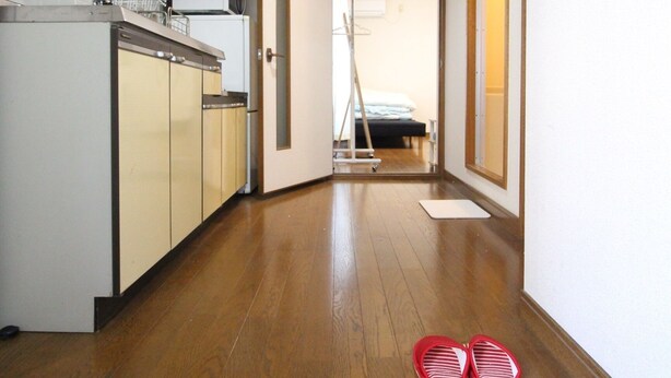 A narrow hallway with wooden flooring, a kitchen area on the left, and a bedroom visible through an open door. - Furere Shichijo (Kyoto)