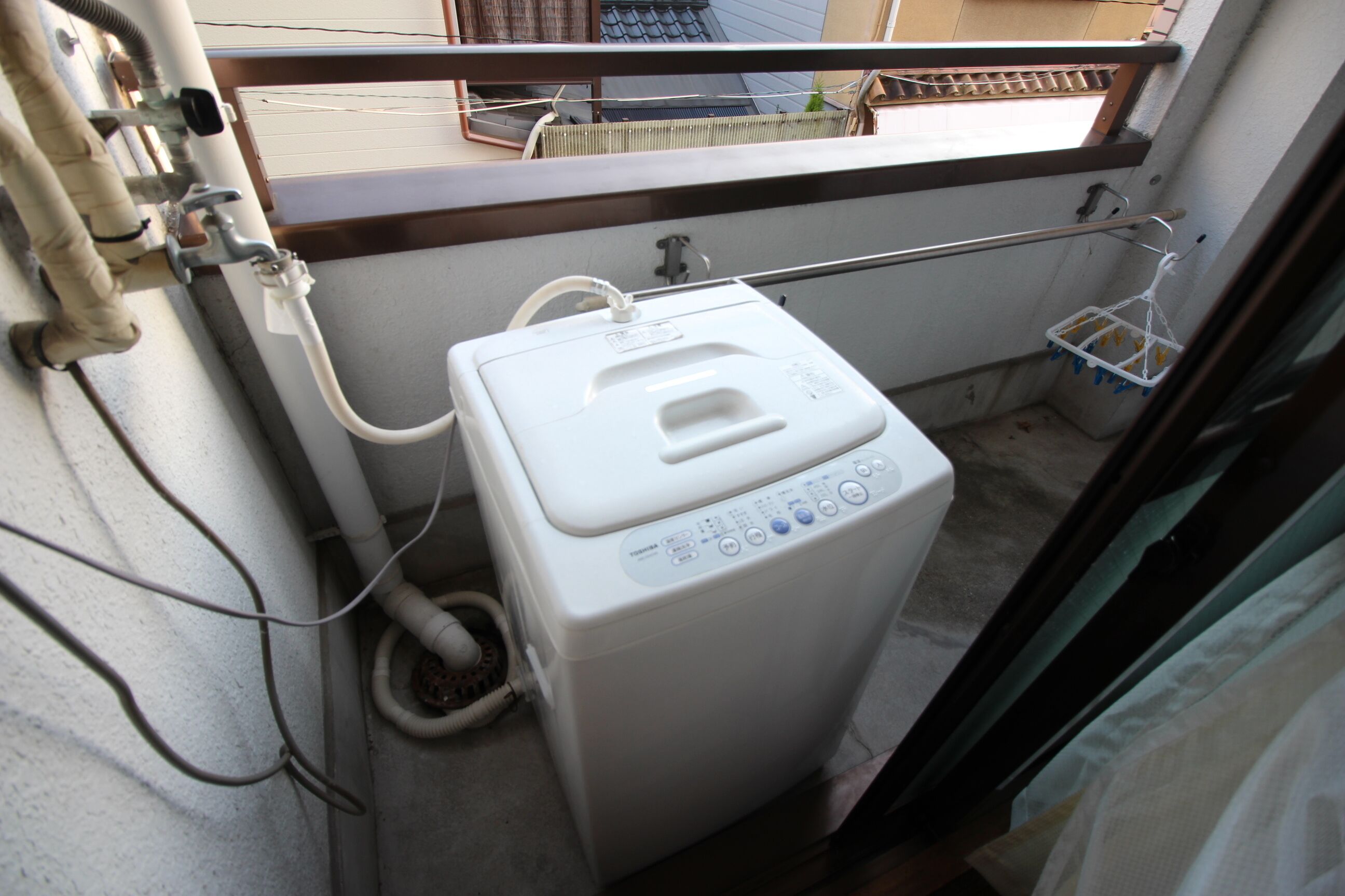 A compact, white, front-loading washing machine with a control panel, connected to a hose and a wall-mounted pump.